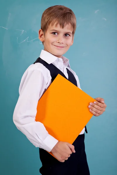 Cute schoolboy is holding an orange book — Stock Photo, Image