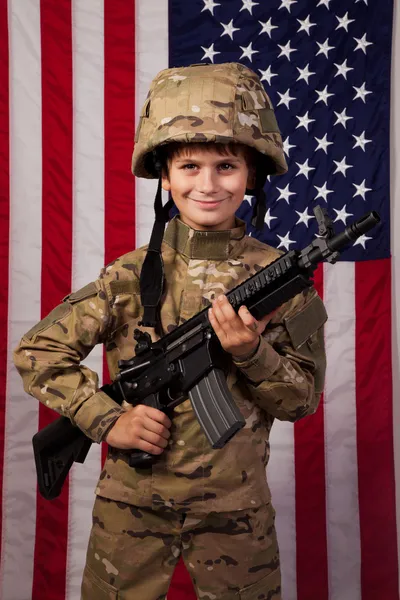 Boy USA soldado na frente da bandeira americana com rifle — Fotografia de Stock