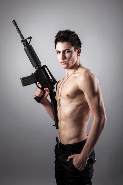 Handsome bare-chested soldier is holding a rifle — Stock Photo, Image