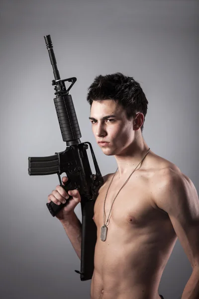 Un guapo soldado de pecho desnudo sostiene un rifle — Foto de Stock