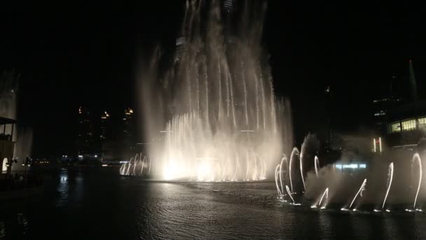 Fountain near Burj Khalifa illuminated by the city at night — Stock Video