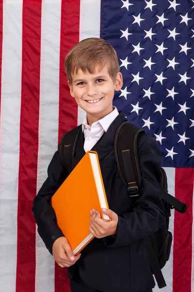 Netter Schuljunge hält ein Buch gegen die US-Flagge — Stockfoto