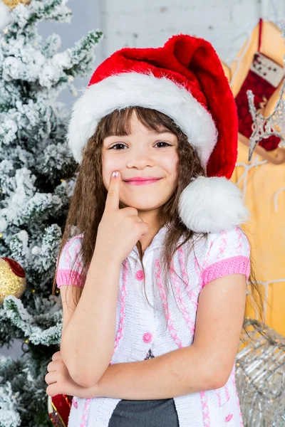 Glad liten tjej i santa hatt framför granen — Stockfoto