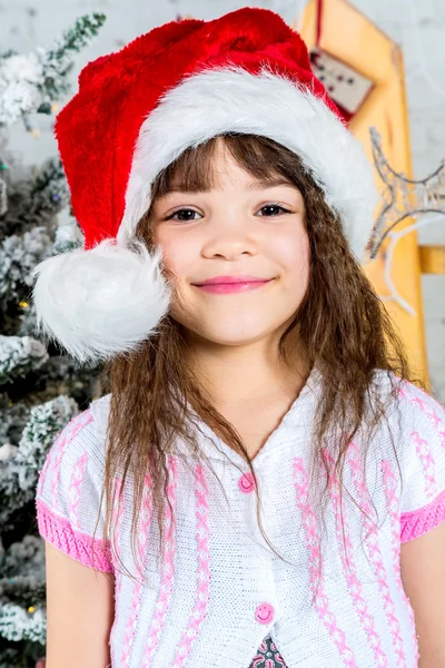 Šťastná holčička v santa klobouk před vánoční stromeček — Stock fotografie