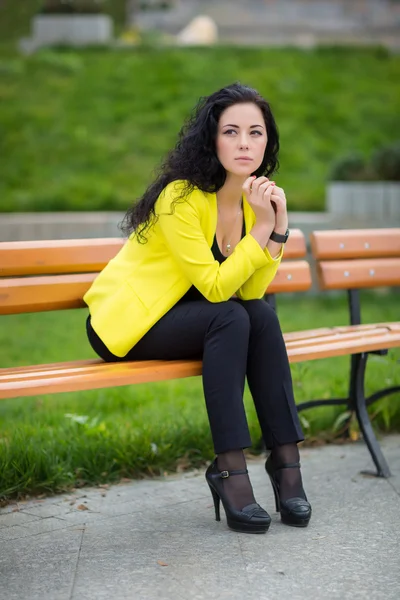 Довольно грустная молодая женщина с длинными вьющимися волосами сидит в парке — стоковое фото