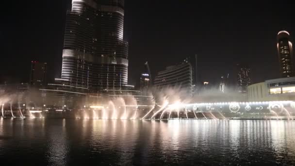 Fontein in de buurt van burj khalifa verlicht door de stad bij nacht — Stockvideo