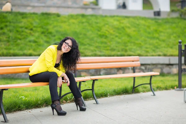 Menina bonita está sentada em um banco de parque — Fotografia de Stock