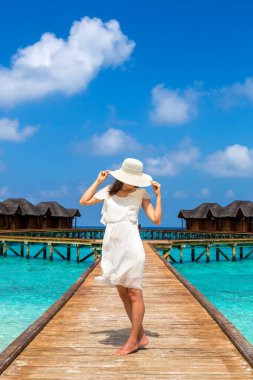 Maldivler adasındaki tropikal sahil iskelesinde (ahşap iskele) duran su lüks villalarının önünde duran güzel genç bir kadın.