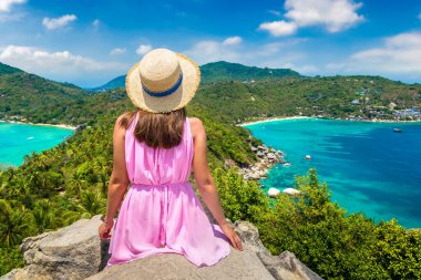 Tayland 'daki Koh Tao adasının panoramik hava manzaralı pembe elbiseli ve hasır şapkalı kadın gezgin.