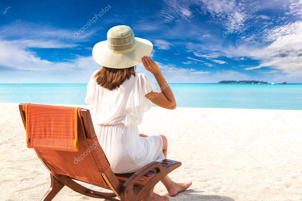 Beautiful woman relaxing in sunbed at luxury tropical beach in a sunny summer day