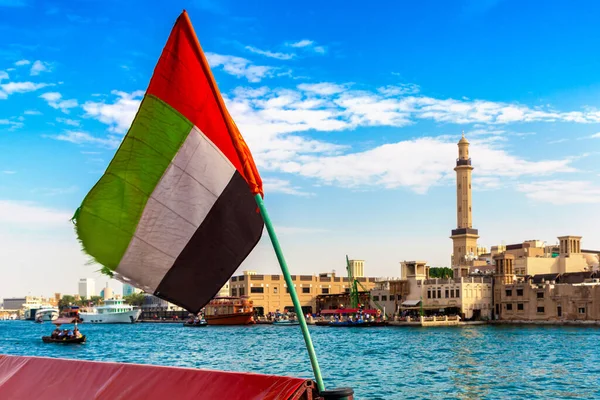 Abra 'ya karşı Birleşik Arap Emirlikleri bayrağına odaklan. Eski ahşap tekne ve Dubai Körfezi' ndeki Dubai Mescidi Camii.