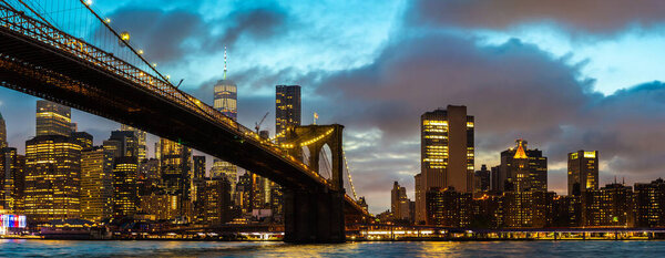 Panorama of Brooklyn Bridge and panoramic night view of downtown Manhattan after sunset in New York City, USA