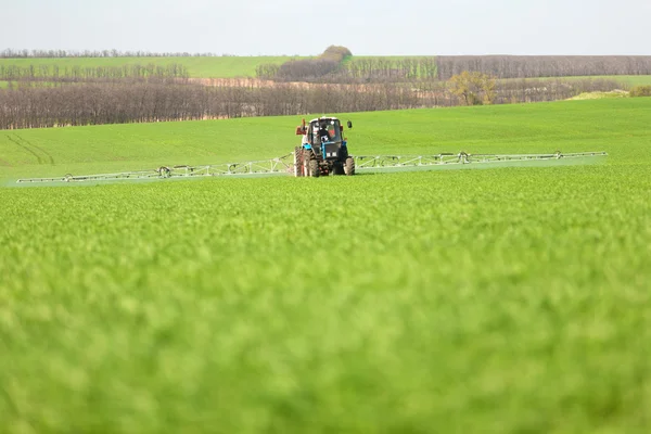 Trator pulverizando um campo verde em uma fazenda — Fotografia de Stock