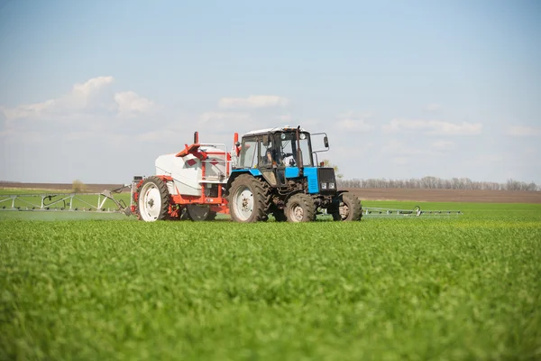 Trator pulverizando um campo verde em uma fazenda — Fotografia de Stock