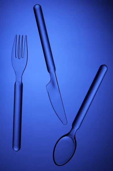 Tenedor transparente, cuchara y cuchillo sobre fondo azul — Foto de Stock