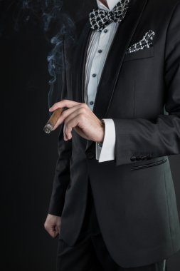 bir puro sol elinde tutan siyah elbiseli adam