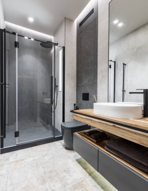 Modern minimalist parlak banyo ahşap mobilyalar, gri ve bej taş fayanslar ve cam duş kabini. İç tasarım kavramı 