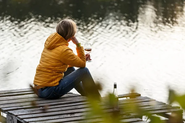 黄色のジャケットを着た女性が湖の上の木製の桟橋でリラックスし 秋の夕日を一人で見ています リラクゼーション 瞑想を楽しむ — ストック写真