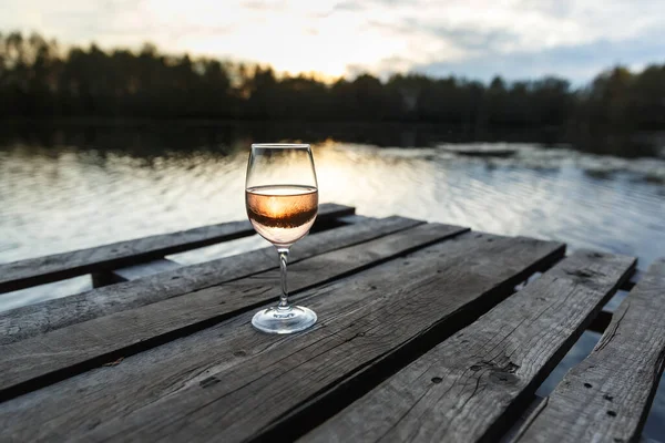 湖の上の木製の桟橋にオレンジワインのガラスの夕日の景色 美しい場所でワインを飲む — ストック写真