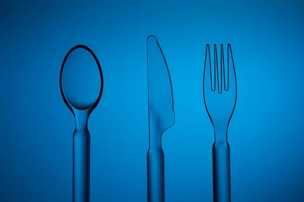 プラスチック透明スプーン ナイフのセットと青の背景にフォーク スタジオショット — ストック写真