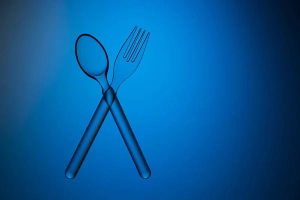 塑料透明勺子和叉子交叉在蓝色的背景上 工作室拍摄 — 图库照片