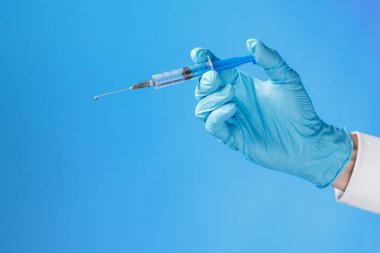 Mavi arka planda bir şırınga tutan mavi lastik bir eldiven verin. Tıbbi enjeksiyon kavramı.