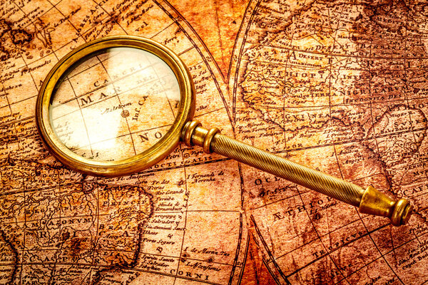 Vintage magnifying glass lies on an ancient world map