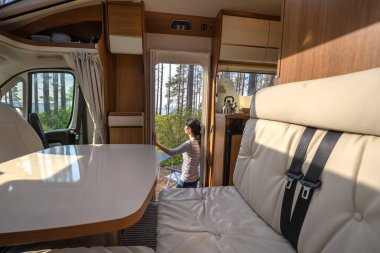 Bir karavan karavanında bir fincan kahveyle doğaya bakan bir kadın. Aile tatili karavanı, karavan tatili, karavan tatili..
