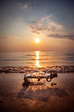 Message in the bottle against the Sun setting down clipart