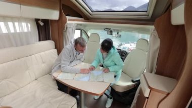 Karavan kampındaki çiftler yolculuk için yerel haritaya bakıyorlar. Aile seyahati, karavan gezisi, karavan tatili..