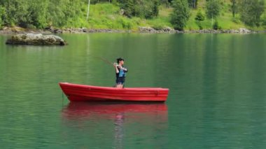 Teknedeki kadın Norveç 'te dönerken balık yakalar. Norveç 'te balık tutmak yerel yaşam tarzını benimsemenin bir yoludur. Sayısız göl ve nehirler ve geniş bir kıyı şeridi olağanüstü fırsatlar demektir.