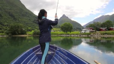 Teknedeki kadın Norveç 'te dönerken balık yakalar. Norveç 'te balık tutmak yerel yaşam tarzını benimsemenin bir yoludur. Sayısız göl ve nehirler ve geniş bir kıyı şeridi olağanüstü fırsatlar demektir.