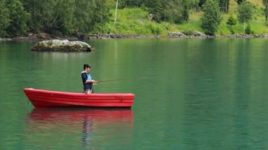 Teknedeki kadın Norveç 'te dönerken balık yakalar. Norveç 'te balık tutmak yerel yaşam tarzını benimsemenin bir yoludur. Sayısız göl ve nehirler ve geniş bir kıyı şeridi olağanüstü fırsatlar demektir.