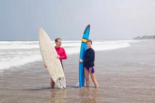 Young with surfboards stand in water