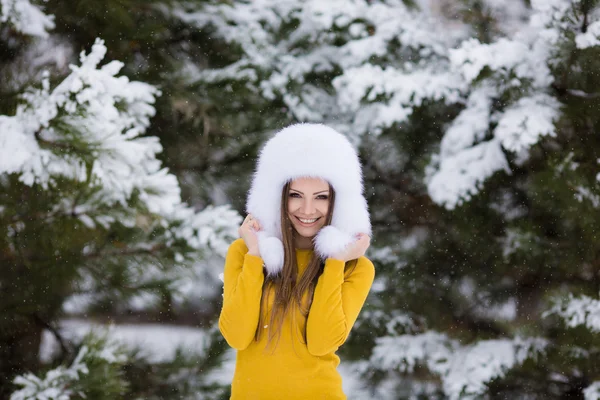 Schöne Mädchen mit einem weißen flauschigen Hut auf Schnee — Stockfoto