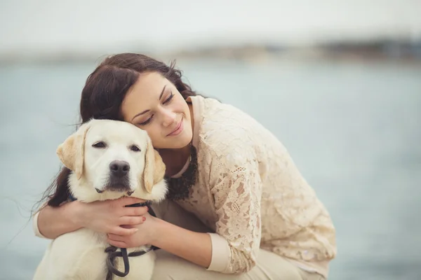 Portrait of beautiful young woman playing with dog on the sea — Stock Photo, Image