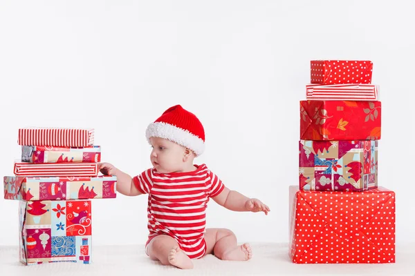 Adorable child in santa cap with stacks of present boxes around — Stock Photo, Image