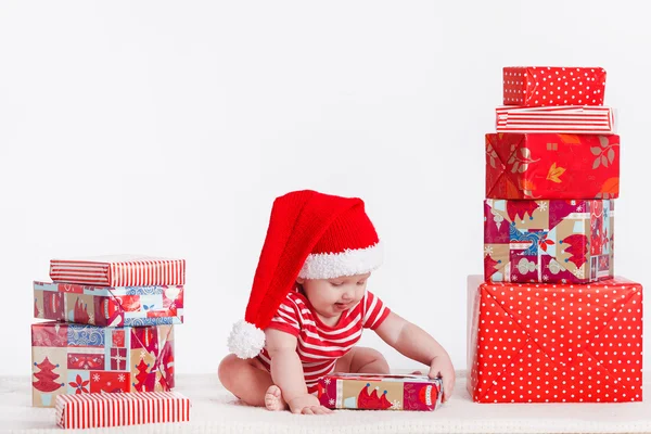 Adorable child in santa cap with stacks of present boxes around — Stock Photo, Image