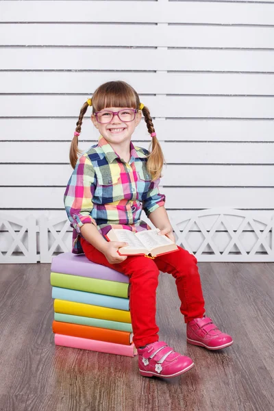 Kleines Mädchen sitzt auf Bücherstapel — Stockfoto
