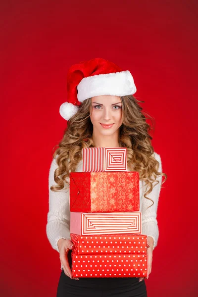 Attractive girl in Santa hat with gifts isolated on red — Stock Photo, Image