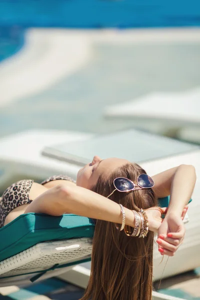 Vrouw zonnebaden in bikini in tropische vakantie resort. mooie jonge vrouw liggen op een ligstoel in de buurt van zwembad — Stockfoto