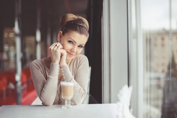 Mujer joven y bonita sentada en un café con una taza de café con leche —  Fotos de Stock