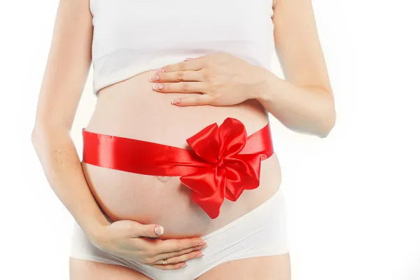 Portrait of Pregnant woman holding pair of red tiny shoes for baby on red background. Studio — Stock Photo, Image