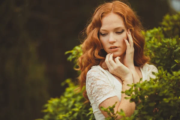 Портрет молодой красивой рыжей женщины, стоящей в зеленом летнем парке — стоковое фото