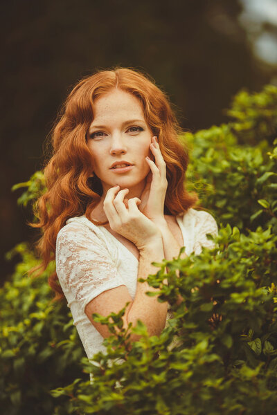 Портрет молодой красивой рыжей женщины, стоящей в зеленом летнем парке
