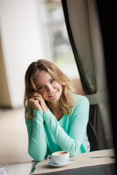 Retrato de una linda rubia sonriente sentada en un café con una gorra de café —  Fotos de Stock