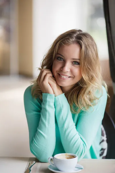 Retrato de uma linda mulher sorrindo loira sentada em um café com um boné de café — Fotografia de Stock