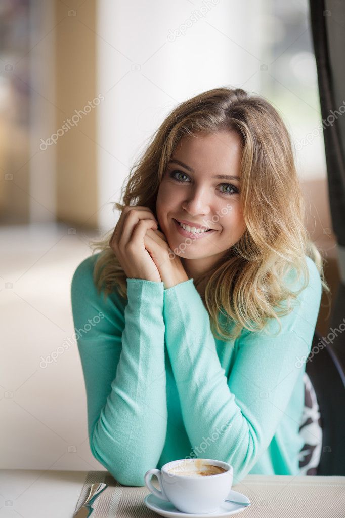 Portrait of a cute blonde smiling woman sitting in a cafe with a cap of coffee