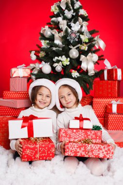 Noel hediyeleri gülümseyerek mutlu ve heyecanlı holding santa şapka Noel kız portresi. şirin mükemmel Noel Baba çocuğun kırmızı zemin üzerine.