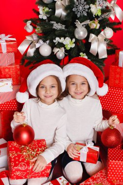 Noel hediyeleri gülümseyerek mutlu ve heyecanlı holding santa şapka Noel kız portresi. şirin mükemmel Noel Baba çocuğun kırmızı zemin üzerine.